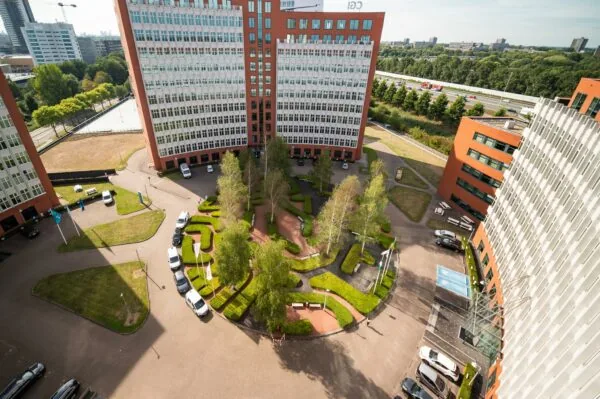 Luchtfoto van het kantoorgebouw aan de George Hintzenweg met centraal een groen aangelegde binnentuin en omliggende parkeerplaatsen.